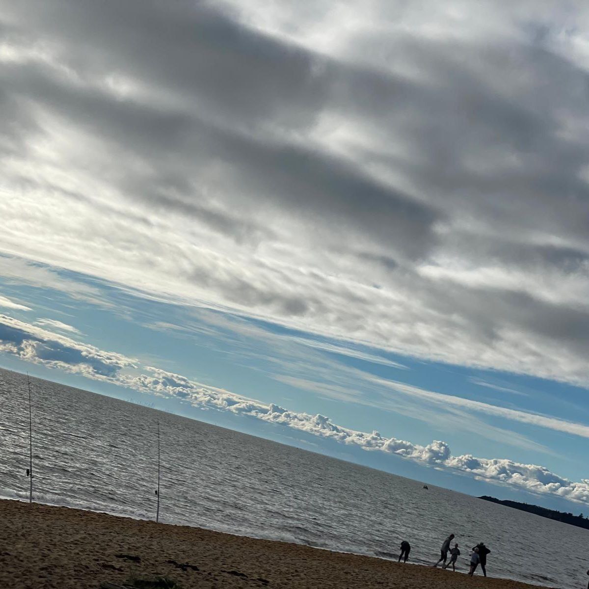 Cloudy sky above a beach with people walking near the water, breezy day