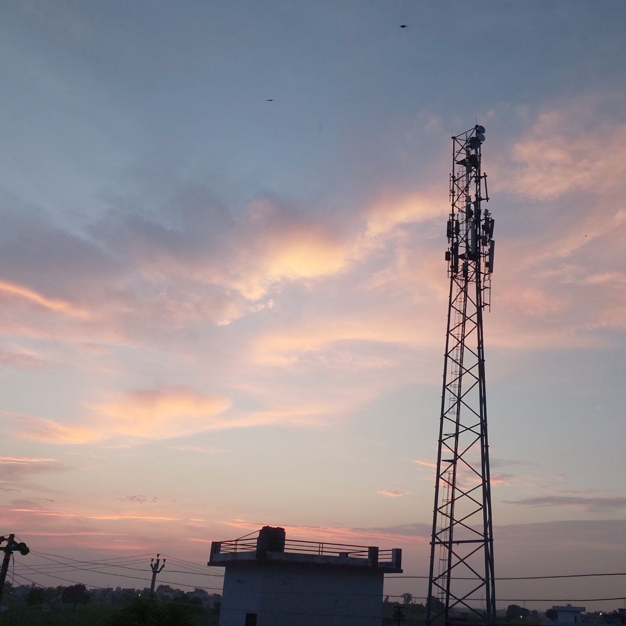 Colourful evening sky with dark clouds and a tall metal tower, soft sunset colours