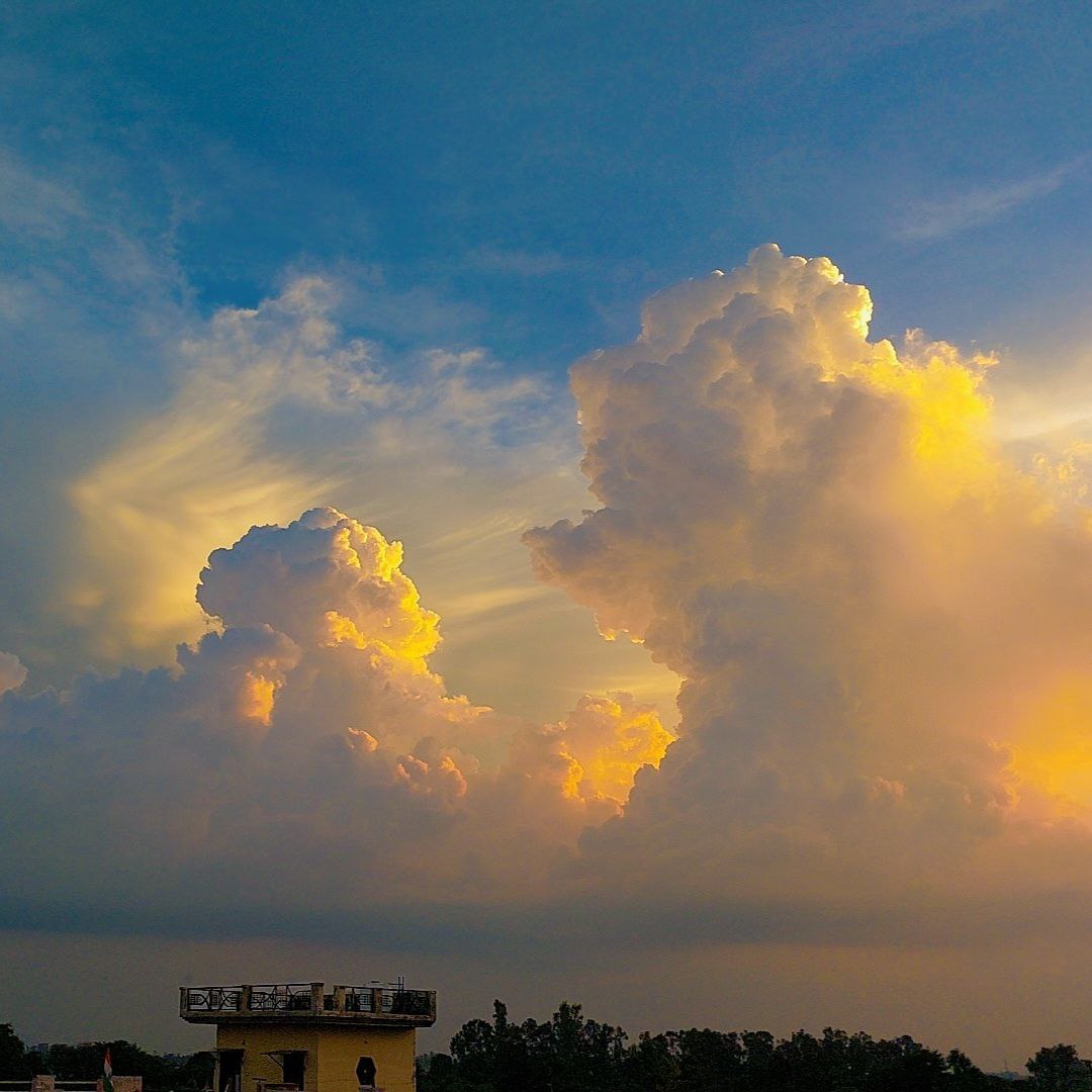 Fluffy golden clouds shining in the bright blue sky, warm sunlight