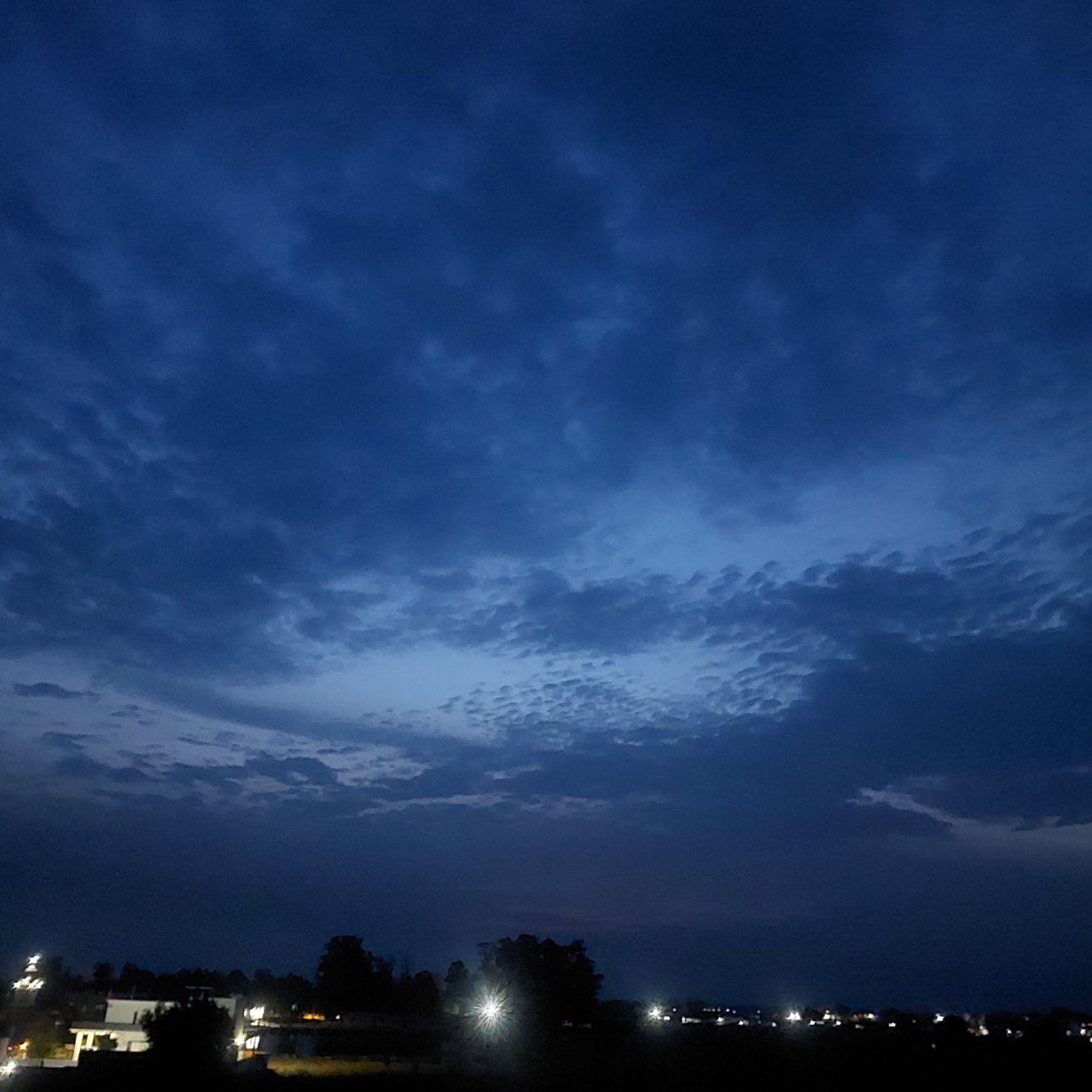 Vibrant view of a dramatic blue sunset sky with scattered clouds over a distant city, atmospheric evening photography for Golden Landscapes gallery