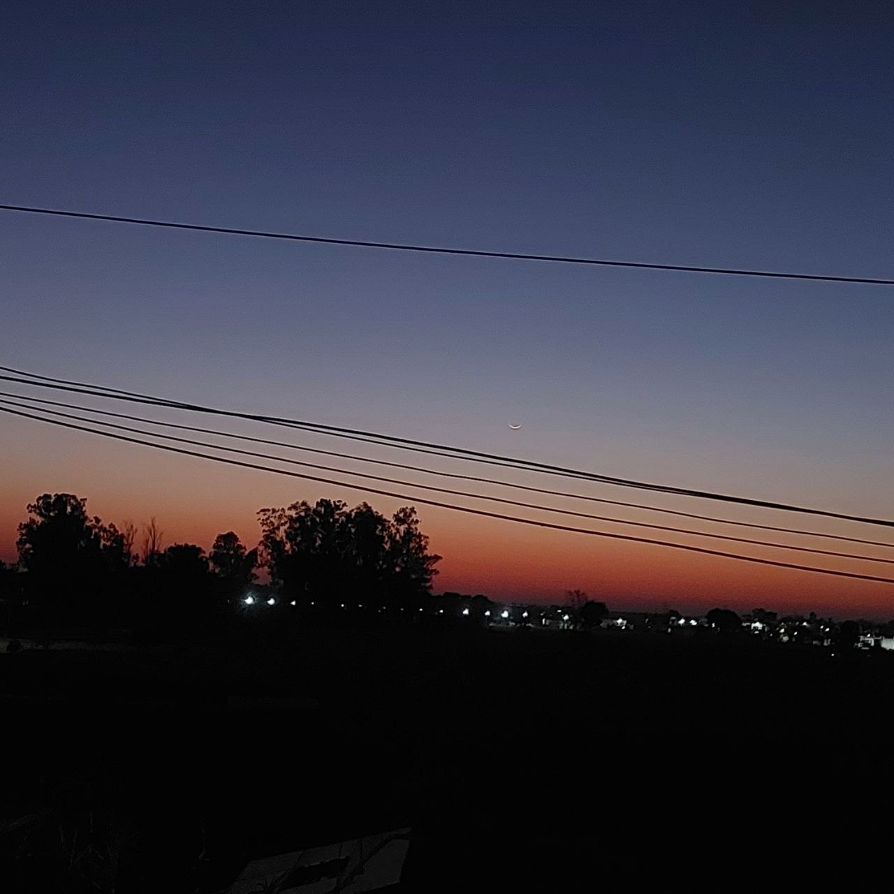 Deep blue and orange hues spreading across the sky at nightfall with distant trees and rooftops, calming evening nature photography for Golden Landscapes gallery